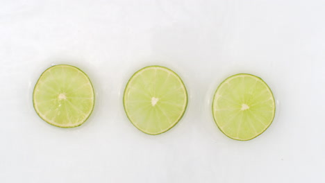 Splashes-of-water-fall-on-sliced-lime-green-rings-on-a-white-background.-Super-slow-motion.